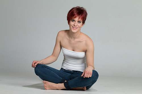 Model, das mit der GFH-Perücke „Vicky Flame Mix“ mit überkreuzten Beinen auf dem Boden sitzt und in die Kamera lächelt