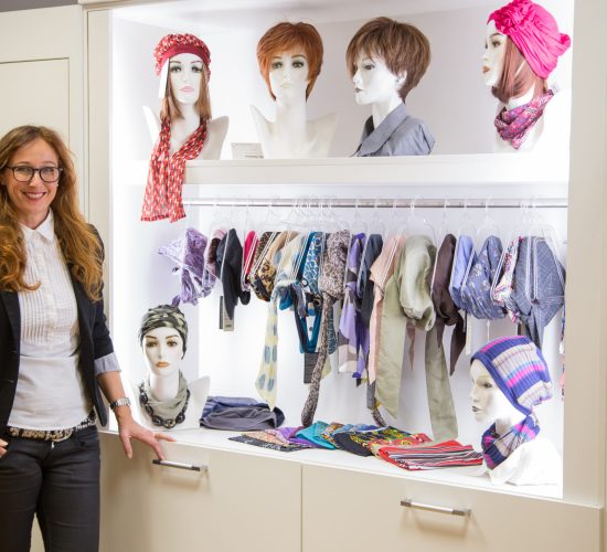 Frau Overmann im Zweithaarstudio vor Turbanen und Perücken